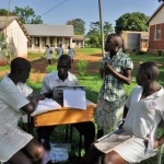 One of our students, Kaka, takes the notes on his Brailler from a sighted girl.