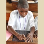 Solomon, visually impaired, using a slate and stylus to take notes